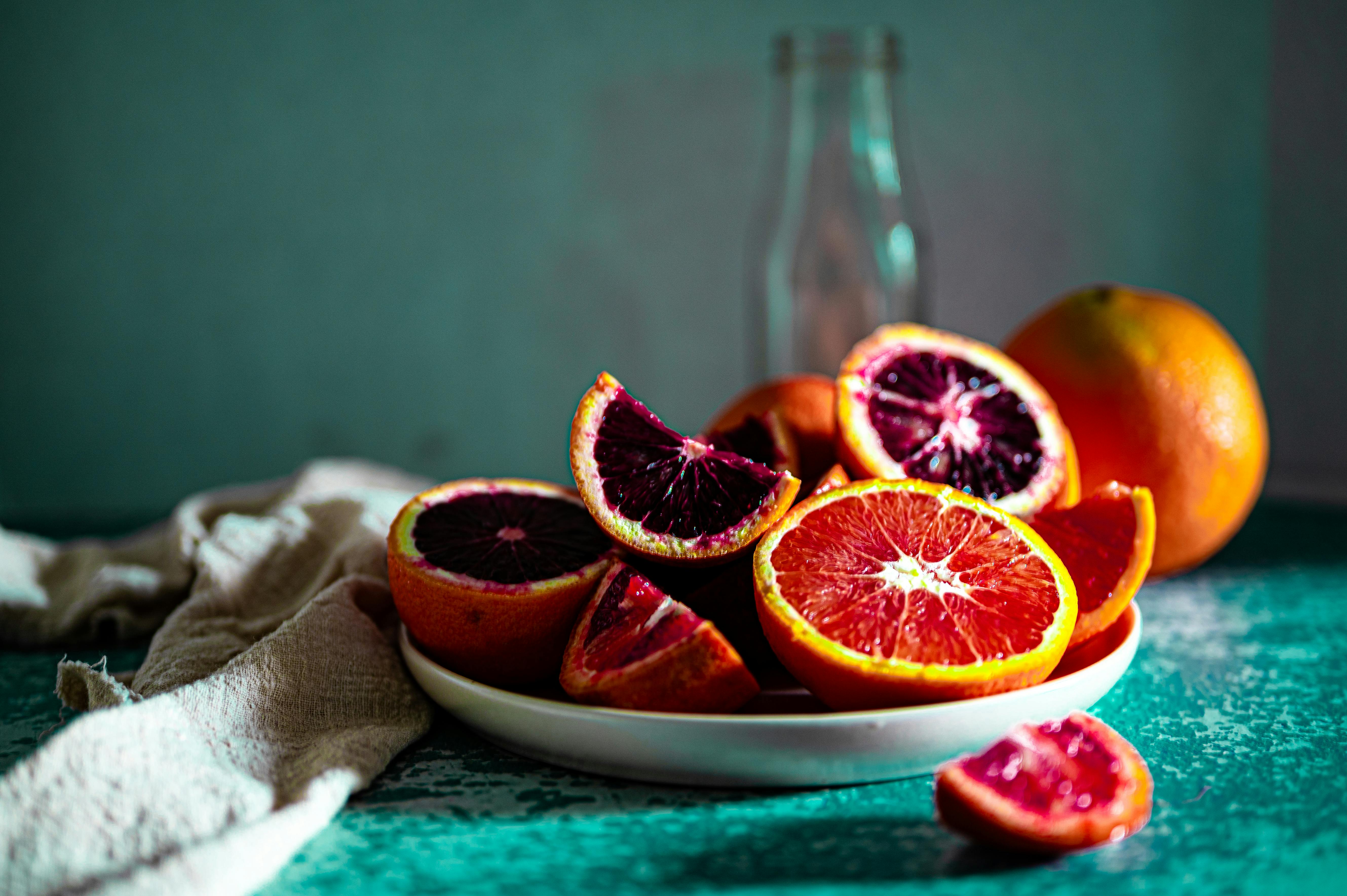 Bowl of whole and halved blood oranges, showing deep ruby and bright orange flesh against a dark background.